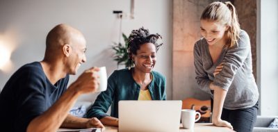 Empresarios felices mirando el portátil mientras toman un café durante una reunión en una oficina creativa.