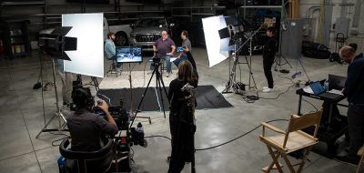 Production crew filming a video of three people talking in front of two trucks.